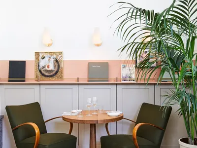 Modern restaurant seating area with green upholstered chairs, wooden table, and decorative plant.