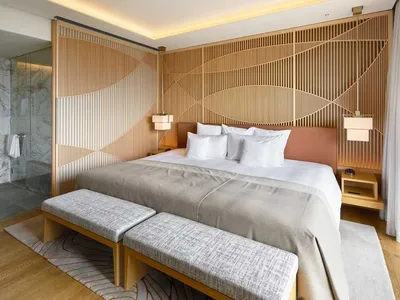 A modern minimalist bedroom featuring a wooden panel wall with geometric patterns, a glass-enclosed shower area, and marble f