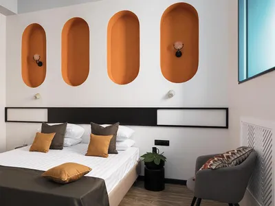 A minimalist bedroom featuring a large bed with white bedding, brown and orange decorative pillows, and orange wall niches.