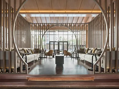 Modern industrial hotel lounge with wooden and concrete materials, featuring seating areas, tables, and a large window.