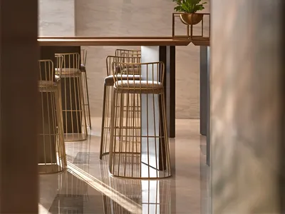 Modern restaurant interior with glass chandelier, wooden table, and brass stools.