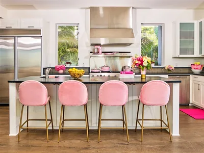 A modern kitchen with sleek metallic finishes and pink velvet cushioned stools.