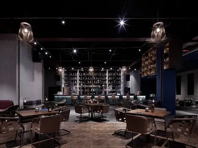 A modern restaurant bar with concrete walls and leather seating, featuring a well-lit central area with tables and chairs.