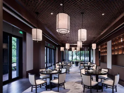 A modern restaurant interior with round tables, white chairs, large windows, and a decorative ceiling.