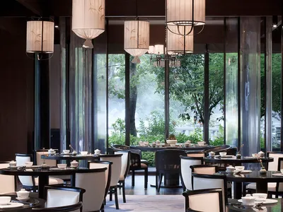 A modern restaurant interior with elegant lighting fixtures and large windows showcasing greenery.