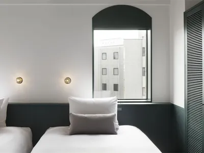 A minimalist hotel room with white walls and bedding.