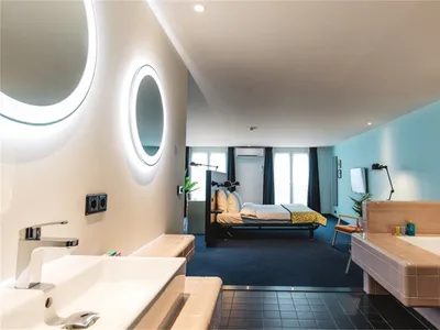 Contemporary hotel room featuring modern furnishings, tiled flooring, concrete accents, and a spacious layout with a bed, sin