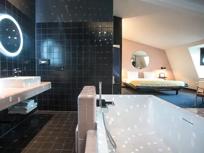 A modern hotel room featuring black tiled walls, a white bathtub, and a double bed.