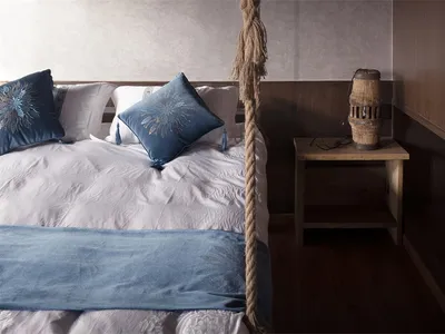 A minimalist bedroom featuring blue and white textiles, a wooden headboard, and a wooden bedside table with a decorative ligh