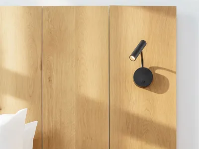 Minimalist bedroom with a bed, white pillows, and a wall-mounted bedside lamp with wooden panels.
