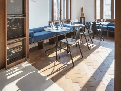 A modern restaurant interior with wooden flooring, blue upholstered seating, and marble accents.