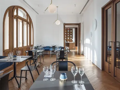 Modern restaurant interior with wooden floors, tables, and chairs, featuring a contemporary design with white walls and large