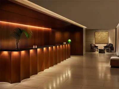 Modern, luxury hotel reception area with wooden finishes, illuminated by warm, ambient lighting, featuring a sleek, minimalis