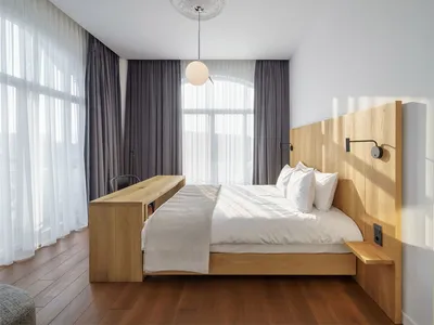 Modern minimalist bedroom with a wooden floor, bed, and chairs, featuring a light pendant chandelier and large windows with s