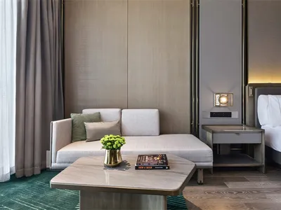 A modern minimalist hotel room featuring a comfortable seating area, a side table with a vase and a book, and a bed.