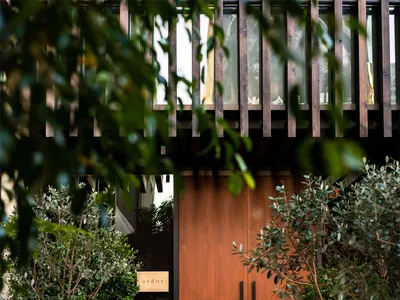 A modern restaurant entryway with wooden doors and lush greenery surrounding them.