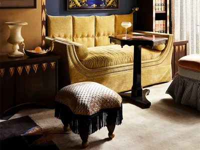 A cozy, eclectic living room with a yellow velvet sofa, bookshelves, and various decorative elements.