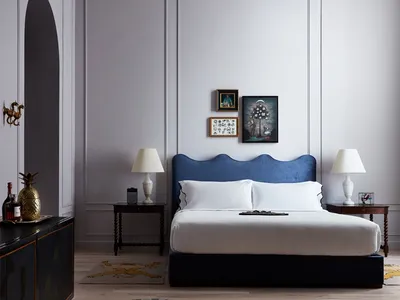 A modern minimalist bedroom with a blue upholstered headboard, wooden flooring, and framed art on the wall.