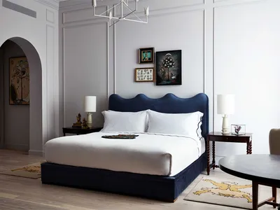 A minimalist bedroom with a white bed, blue headboard, and framed art on the wall.