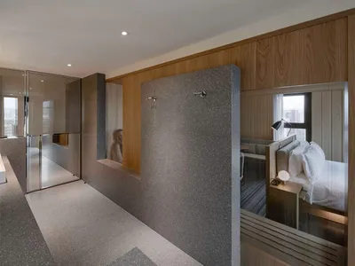 Modern hotel room with concrete walls and floor, minimalist design, and sliding glass doors.