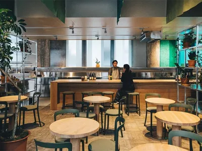 Industrial-style restaurant interior with wooden tables, concrete flooring, and metal bar counter.