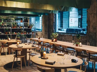 Interior of a modern food court with wooden tables and chairs, greenery, and a wine rack.