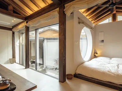 A modern minimalist bedroom with a white bed, wooden frame, and circular window.