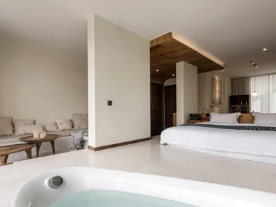 A minimalist bedroom with a white bed, wooden accents, and a bathtub.
