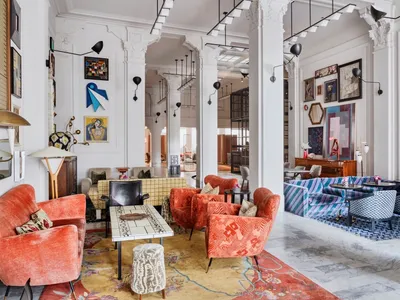 A modern hotel lounge with patterned fabric seating, wooden tables, and various artwork on the walls.