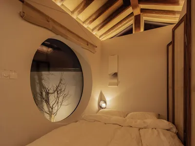A minimalist bedroom with a wooden bed and a circular window