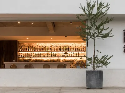 A modern restaurant bar with a concrete façade and illuminated shelves showcasing numerous bottles.