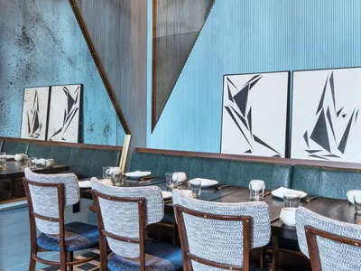 Modern restaurant interior with wooden flooring, metallic chairs, and plaster walls