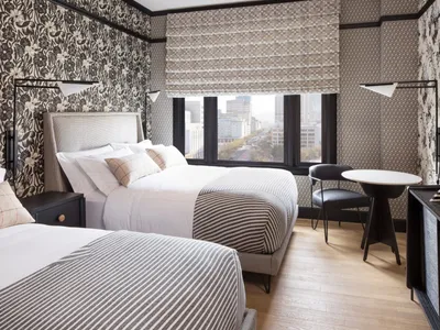 A modern hotel room featuring a bed with striped bedding and a window overlooking a cityscape, complemented by textured wallp