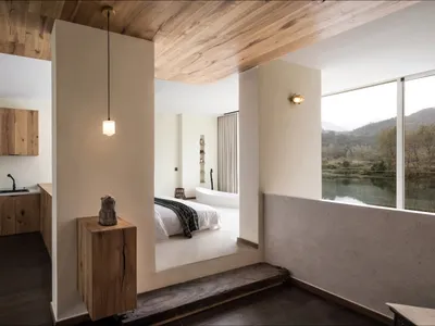 Modern minimalist bedroom featuring a bed with a wooden headboard and a wooden floor, with a view of the mountains through th