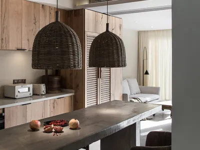 A modern minimalist kitchen with a concrete countertop, featuring a long rectangular table with a bowl of pomegranates and tw