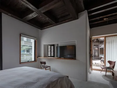 Minimalist bedroom with concrete walls, wood ceiling beams, and a television mounted on a floating shelf.
