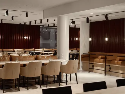 Modern restaurant interior with tables, chairs, and stylish decor made of wood, leather, and metal.