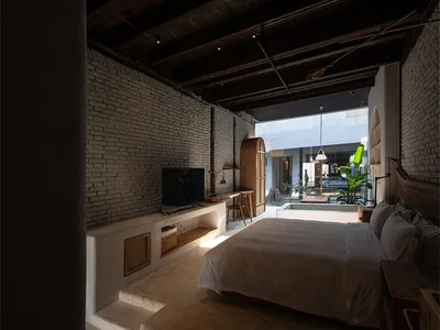 A minimalist bedroom featuring brick walls, concrete flooring, and wooden furniture.