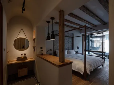 A minimalist bedroom with a white bed, wooden frame, and hanging lamps.