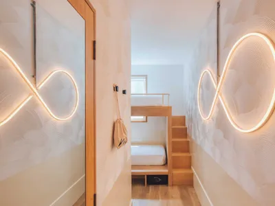 Minimalist bedroom with wooden bunk bed, metallic railing, and textiles.