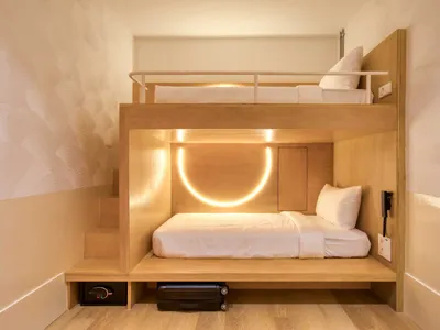 Modern minimalist hotel room with a wooden bunk bed and illuminated lighting.