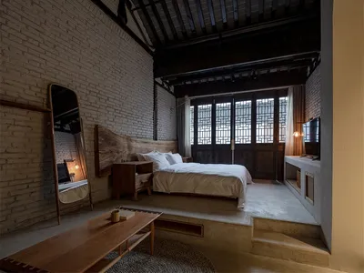 Minimalist bedroom with brick and wooden walls, featuring a cozy bed with white bedding and a wooden table.