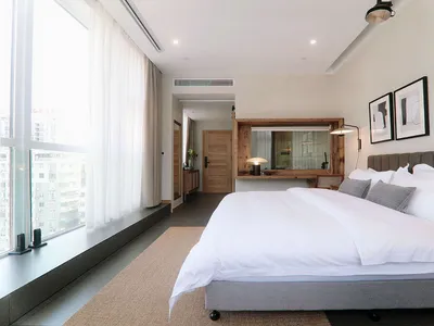 A minimalist bedroom featuring a large white bed, grey headboard, and white walls.