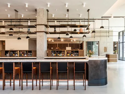 Modern industrial bar with marble countertops, metal stools, and a concrete pillar.