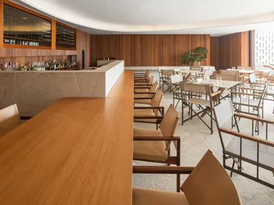 An elegant restaurant bar with wooden chairs, marble countertops, and a curved wooden wall.