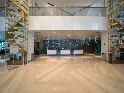 A spacious hotel lobby featuring metallic glass and marble reception counters, illuminated by modern lighting and sleek furni