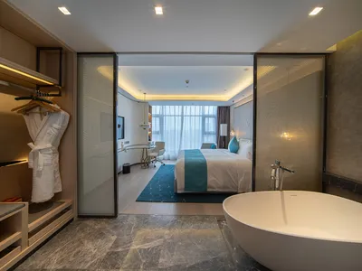Modern hotel suite featuring a marble bathroom and bedroom area with a large bathtub and white furniture.