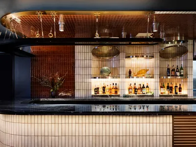 A modern restaurant bar with white and brown marble walls and flooring, featuring a circular hanging light fixture and bottle