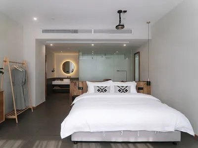 簡約臥室內有一張白色床鋪，搭配幾何圖案枕頭、木質床頭板，以及背景的玻璃隔間。