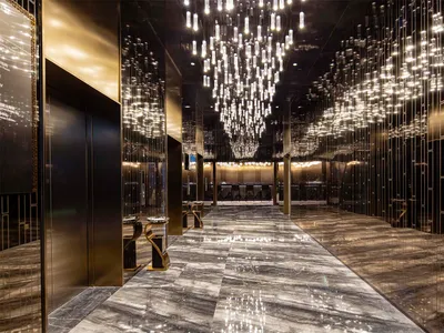 A luxurious hotel lobby featuring marble flooring, hanging chandeliers, and modern lighting fixtures.